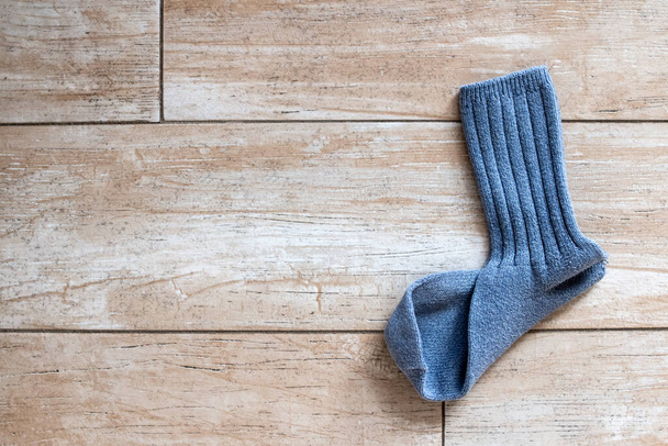 eine einzelne gerippte Socke aus blauer Wolle, die ihren Partner vermisst, liegt auf einem goldbeigen Fliesenboden, der im Sonnenlicht in toronto, ontario, canada, Februar 2021 gebadet ist. - Foto, Bild