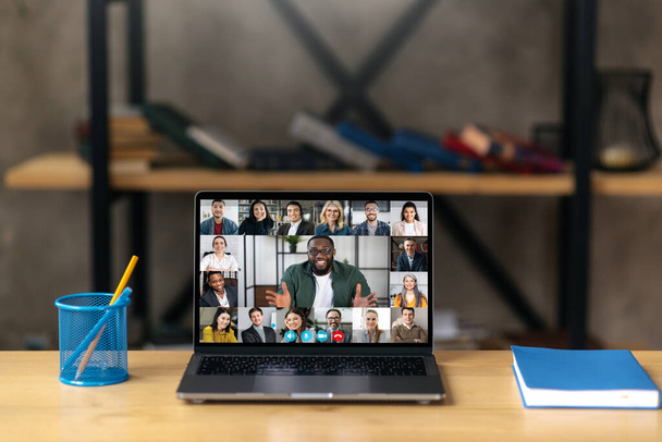 Online business briefing, brainstorm. A laptop stands on the desktop, on the laptop screen is many different multiracial coworkers, gathered, communication, solving working issues - Photo, Image