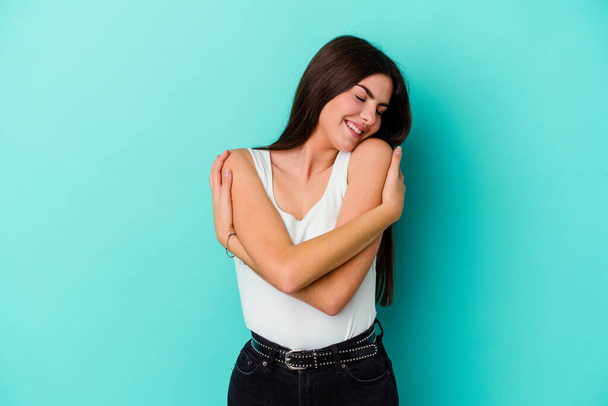 Young caucasian woman isolated on blue background hugs, smiling carefree and happy. - Foto, Bild