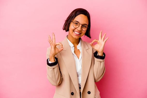 jong bedrijf gemengde ras vrouw geïsoleerd op roze achtergrond vrolijk en zelfverzekerd tonen ok gebaar. - Foto, afbeelding