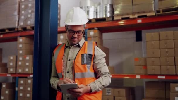 Kaukasischer Mann kontrolliert Geschäftsleute auf digitalem Tablet lächelnd, wie er neben verpackten Paketen im Lager steht - Filmmaterial, Video