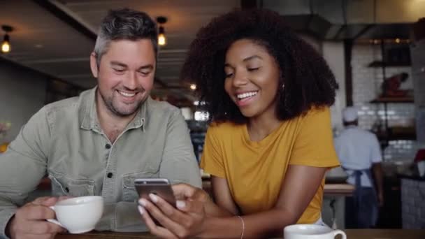 Гарна пара сміється в соціальних мережах пост на смартфоні п'є гарячу каву, сидячи в стильному кафе
. - Кадри, відео
