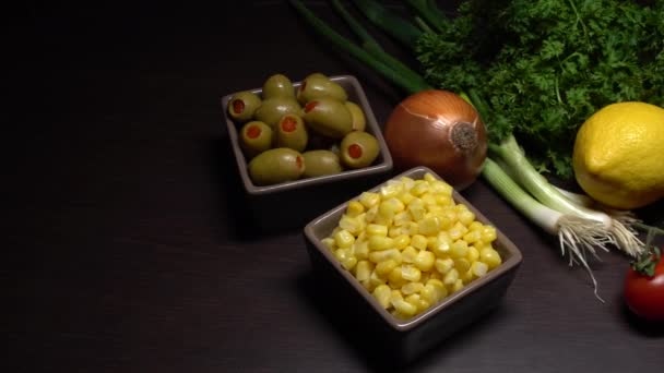 Thon en conserve. Ingrédients pour salade de thon sur un plan de cuisson laitue, olives, oignons de printemps, tomate cerise, maïs, oignon, persil frisé, citron et une boîte de thon ouverte. À droite. Gros plan.   - Séquence, vidéo