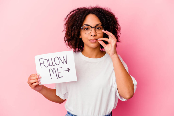 Young african american mixed race woman holding a follow me concept with fingers on lips keeping a secret. - Photo, Image