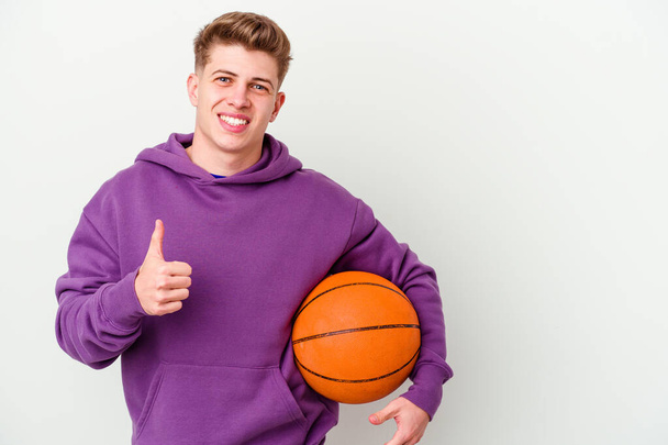 Νεαρός καυκάσιος παίζει μπάσκετ απομονωμένο υπόβαθρο χαμογελώντας και υψώνοντας τον αντίχειρα - Φωτογραφία, εικόνα