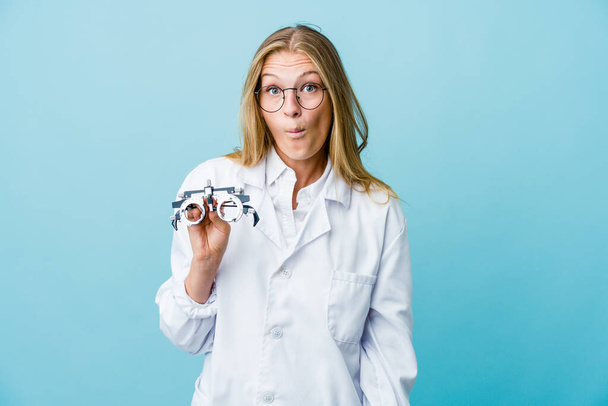 Jovem mulher optometrista russa em ombros de ombros azuis e olhos abertos confusos. - Foto, Imagem