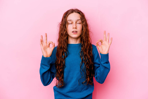 Little caucasian girl isolated on pink background relaxes after hard working day, she is performing yoga. - Фото, изображение