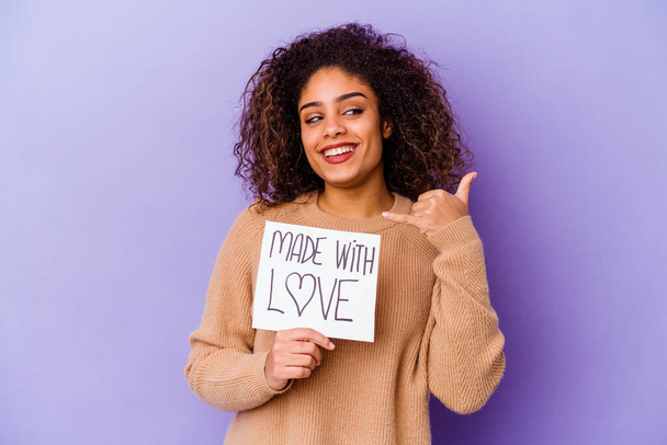 Mladá Afroameričanka drží s láskou plakát izolované na fialovém pozadí ukazující gesto mobilního telefonu s prsty. - Fotografie, Obrázek