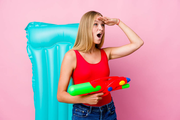 Joven mujer rusa jugando con una pistola de agua con un colchón de aire mirando lejos manteniendo la mano en la frente. - Foto, Imagen