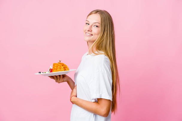 Young russian woman eating a waffle isolated looks aside smiling, cheerful and pleasant. - Foto, immagini