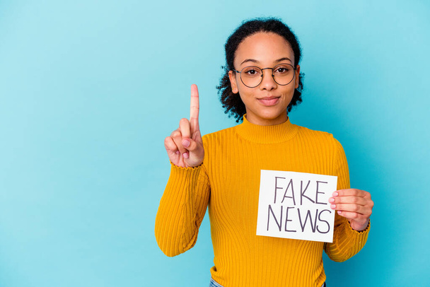 Young african american mixed race woman holding a fake news concept showing number one with finger. - Photo, Image