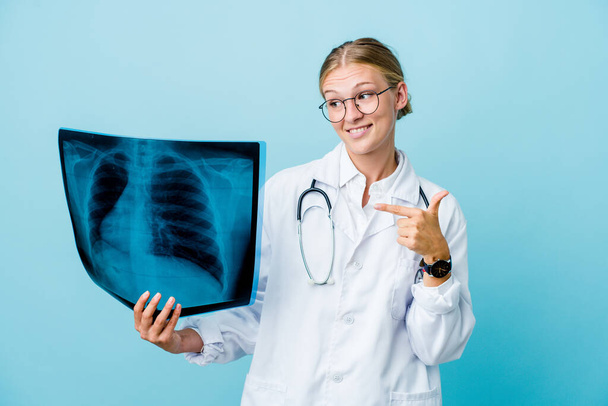 Young russian doctor woman holding a bone scan on blue person pointing by hand to a shirt copy space, proud and confident - Photo, Image