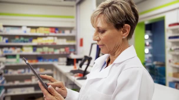 Farmacéutica femenina que clasifica las recetas de medicamentos que se desplazan en la tableta digital de pie con una capa blanca en la phramacy  - Imágenes, Vídeo