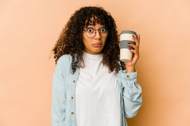 Jeune afro-américaine africaine tenant un café à emporter hausse les épaules et ouvre les yeux confus. - Photo, image