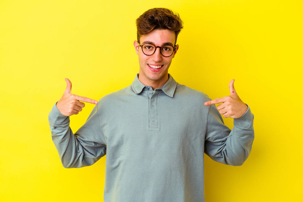 Young caucasian man isolated on yellow background points down with fingers, positive feeling. - Fotoğraf, Görsel
