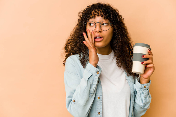 Νεαρή Αφρικάνα Αφρο-Αμερικανίδα που κρατάει καφέ λέει ένα μυστικό καυτό φρένο και κοιτάει στην άκρη. - Φωτογραφία, εικόνα