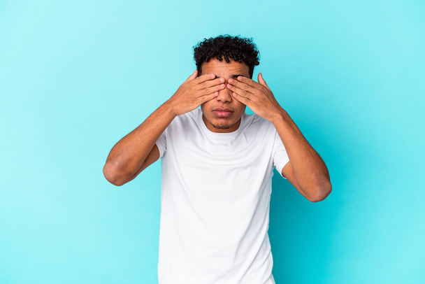 Young african american curly man isolated on blue afraid covering eyes with hands. - Photo, Image