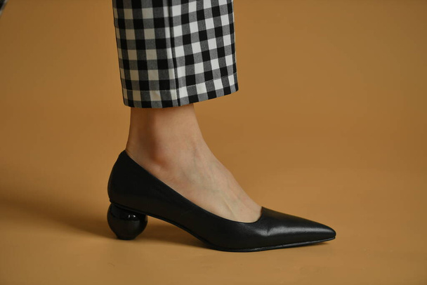 Stylová samičí bota s ostrou ponožkou, jedinečným kuličkovým podpatkem a látkovou mašlí navrchu. Krásné nohavice a kostkované kalhoty. Přírodní barvy a stín, izolované na hnědém pozadí. Módní koncept. - Fotografie, Obrázek