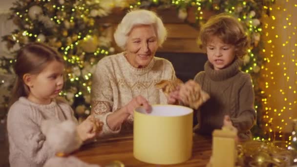 Noel kutusunun süslemesi ve içine hediyeler ve süslemeler koymak için çocukların ve büyükannelerin buruşuk el işi kağıtlarının orta büyüklükte fotoğrafı. - Video, Çekim