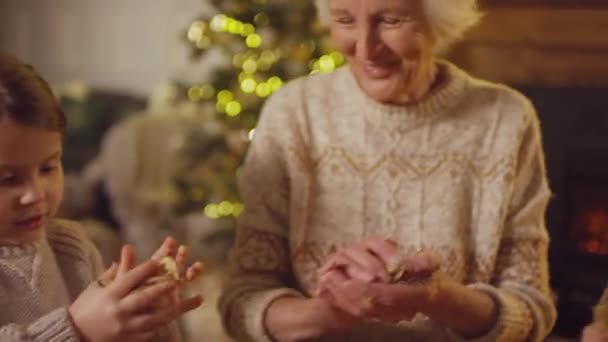 Sluiten van kinderen in gezellige truien verkruimelen ambachtelijk papier helpen oma versieren kerstdoos van speelgoed en decoraties - Video