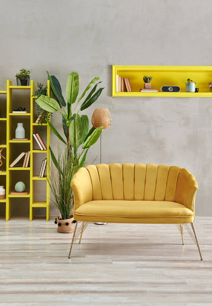 Dekorativní žlutá pohovka nábytek v místnosti, šedá kamenná stěna, žlutá výklenek a knihovna, domácí výzdoba. - Fotografie, Obrázek