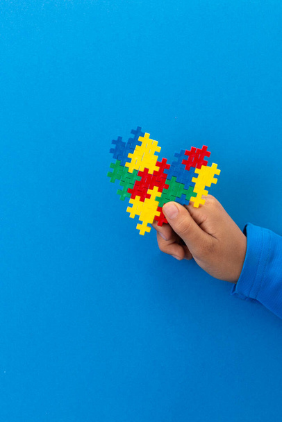 World Autism Awareness Day Konzept. Kinderhand mit buntem Puzzle-Herz auf hellblauem Hintergrund - Foto, Bild