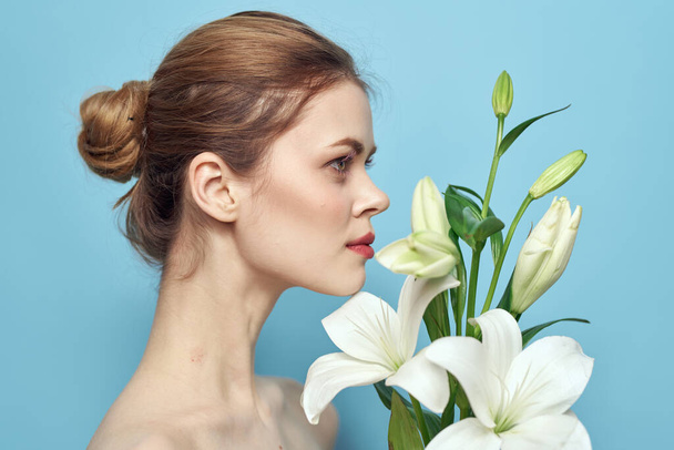 Beautiful girl with a bouquet of white flowers on a blue background cropped view naked shoulders portrait - Photo, Image