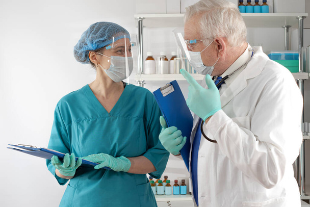 Beyaz önlüklü kıdemli doktor ve kadın sağlık görevlisi belgeleri mavi klasörde inceleyip hastanede tartışıyorlar. - Fotoğraf, Görsel