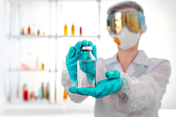 Химик в защитной одежде демонстрирует медицинскую бутылку. Сцена для подражания, копирайт. - Фото, изображение