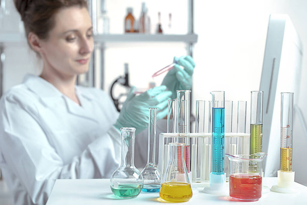 laboratory equipment, supplies, jars, bottles, cylinders, beakers, graduate, test-mixer, medicine-glass. The laboratory assistant makes bacteriological inoculation in a petri dish with a glass stick in defocus - Photo, Image