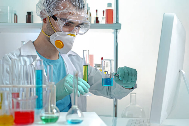 Молодой ученый в защитном оборудовании держит химическую стеклянную посуду. Сцена под открытым небом - Фото, изображение