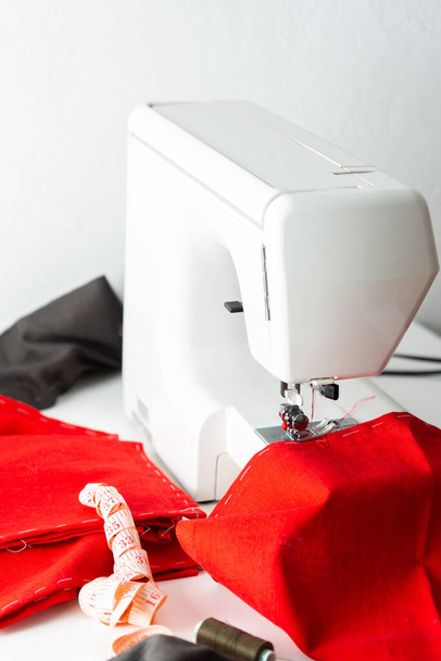 Moderne naaimachine met rode en grijze stof, meetlint en -draad, thuis knippen en naaien, vrije tijd en hobby - Foto, afbeelding