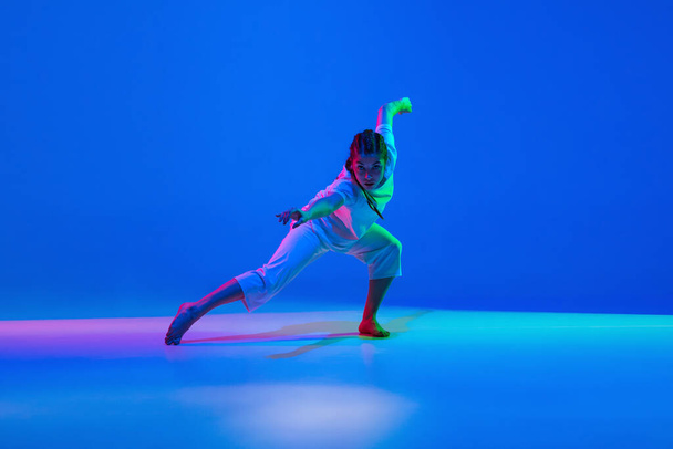 Beyaz elbiseler içinde dans eden genç kız neon ışıklarıyla renkli arka planda. - Fotoğraf, Görsel