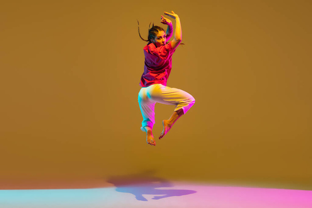 Sportive girl dancing hip-hop in attire on colorful background in neon light - Photo, Image