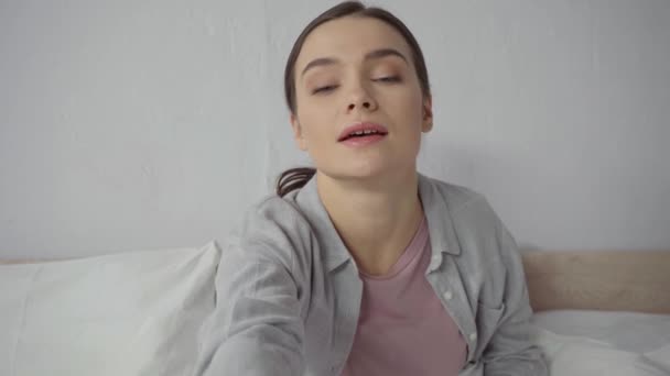 Ευτυχισμένη νεαρή γυναίκα κουνώντας το χέρι κατά τη διάρκεια βιντεοκλήσης στην κρεβατοκάμαρα - Πλάνα, βίντεο