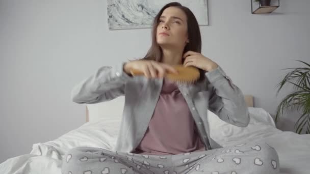 mladá brunetka žena sedí na posteli a kartáčování vlasy - Záběry, video