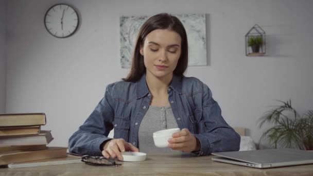jeune femme appliquant de la crème cosmétique sur les mains près d'un ordinateur portable et des livres - Séquence, vidéo