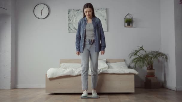 Traurige junge Frau steht auf Waage im Schlafzimmer - Filmmaterial, Video