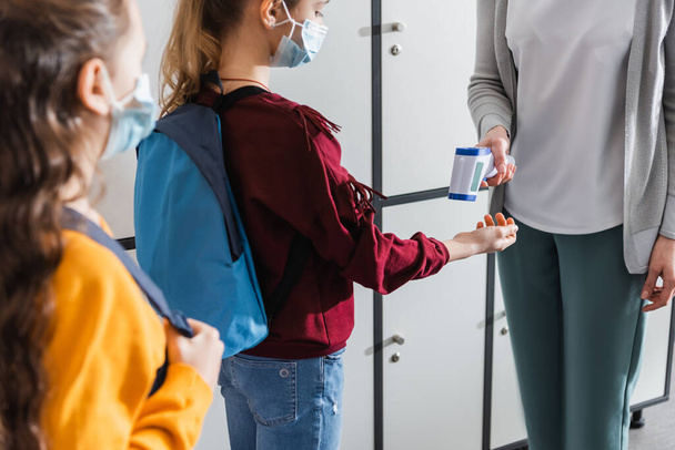 Вчитель з використанням інфрачервоного термометра на шкільному малюку в медичній масці з рюкзаком
  - Фото, зображення