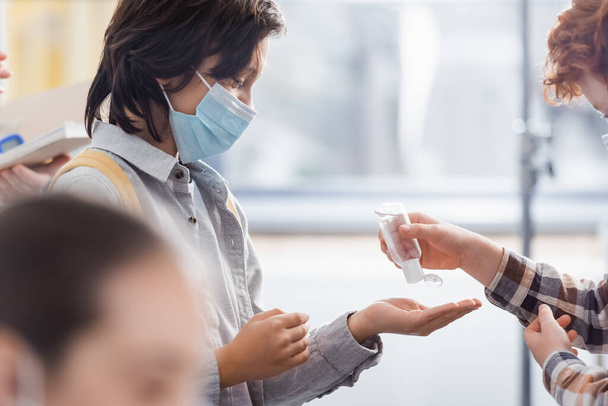 Schuljunge schüttet Desinfektionsmittel auf Hände von Freund in medizinische Maske  - Foto, Bild