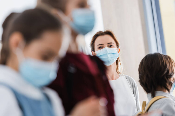 Tanár nézi iskolások orvosi maszkok elmosódott előtérben  - Fotó, kép