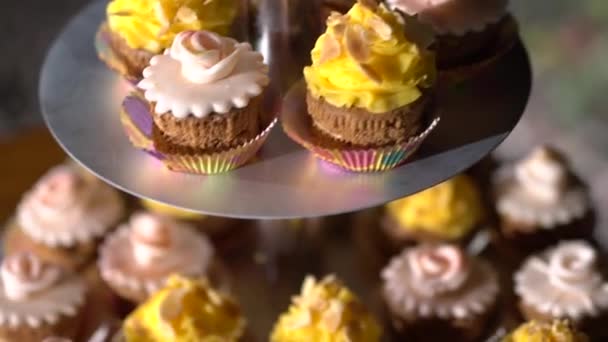 Σταντ με cupcakes διακοσμημένα με κίτρινη και ροζ κρέμα σε εορταστικό δείπνο  - Πλάνα, βίντεο