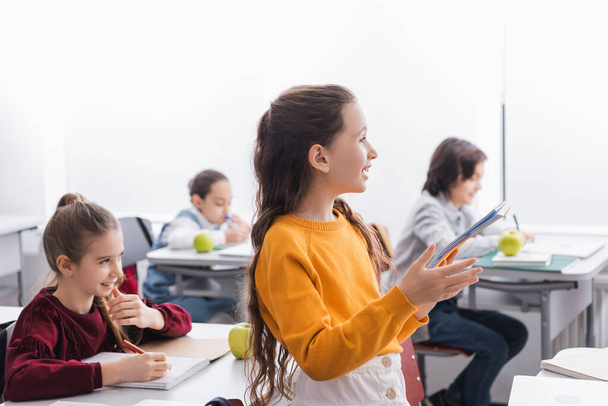 Écolier souriant tenant un cahier pendant les cours en classe  - Photo, image