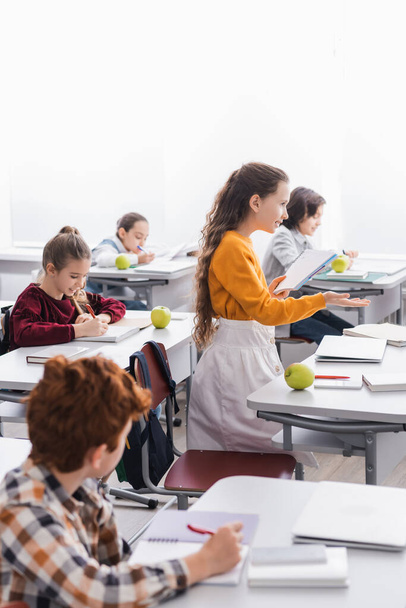 Mosolygó iskolás lány jegyzetfüzetben mutató kézzel közeli barátok írásban notebookok osztályteremben  - Fotó, kép