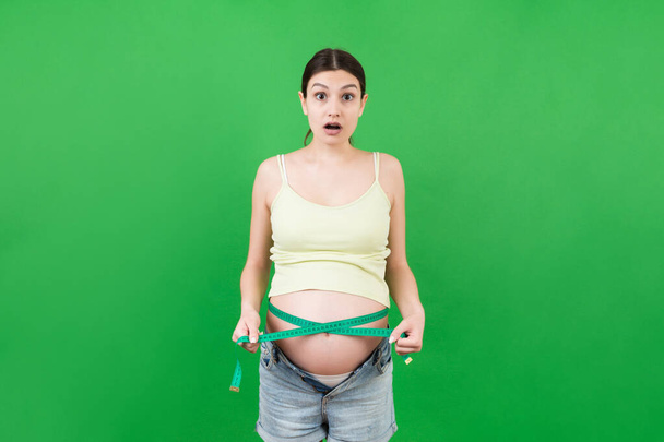 Rajattu kuva odottaa äiti unzipped farkut mittaamalla hänen raskaana vatsa mittanauha värikkäällä taustalla. Senttimetrin mittaus. - Valokuva, kuva