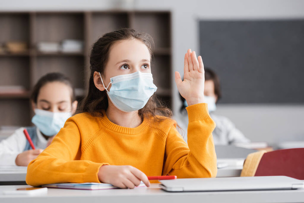 Schülerin in medizinischer Maske hebt während des Unterrichts die Hand - Foto, Bild