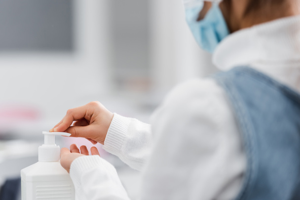 vista recortada de colegiala en máscara médica aplicando desinfectante de manos en primer plano borroso - Foto, Imagen