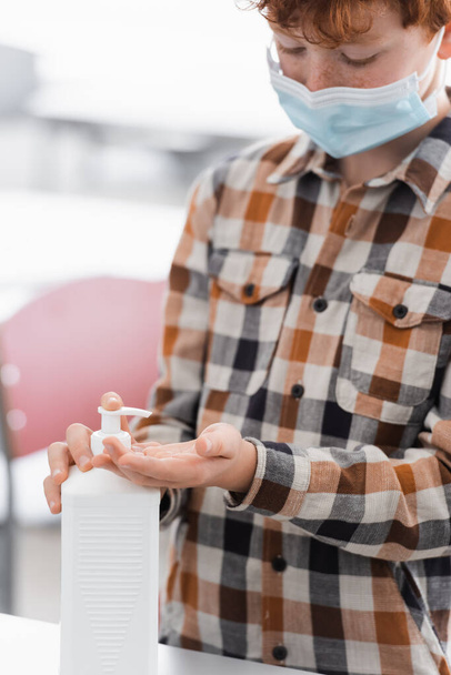 colegial en máscara médica aplicando desinfectante en las manos en la escuela - Foto, Imagen