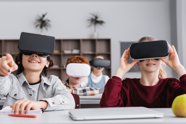 excited boy in vr headset pointing with finger near classmates on blurred background - Photo, Image