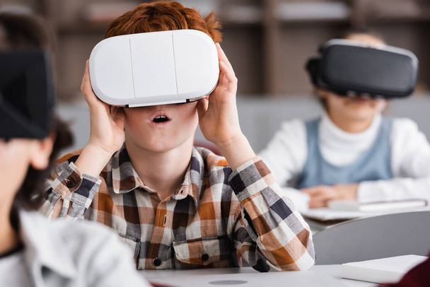 selectieve focus van verbaasd schooljongen gaming in vr headset in de klas - Foto, afbeelding